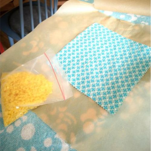 Foto zum ersten Schritt für ein selbstgemachtes Bienenwachstuch: Baumwolltuch auf Backpapier, daneben eine Tüte mit Wachs
