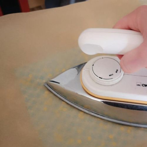 Foto zum dritten Schritt für ein selbstgemachtes Bienenwachstuch: Bügeleisen auf Backpapier, darunter ein mit Wachs bestreutes Tuch