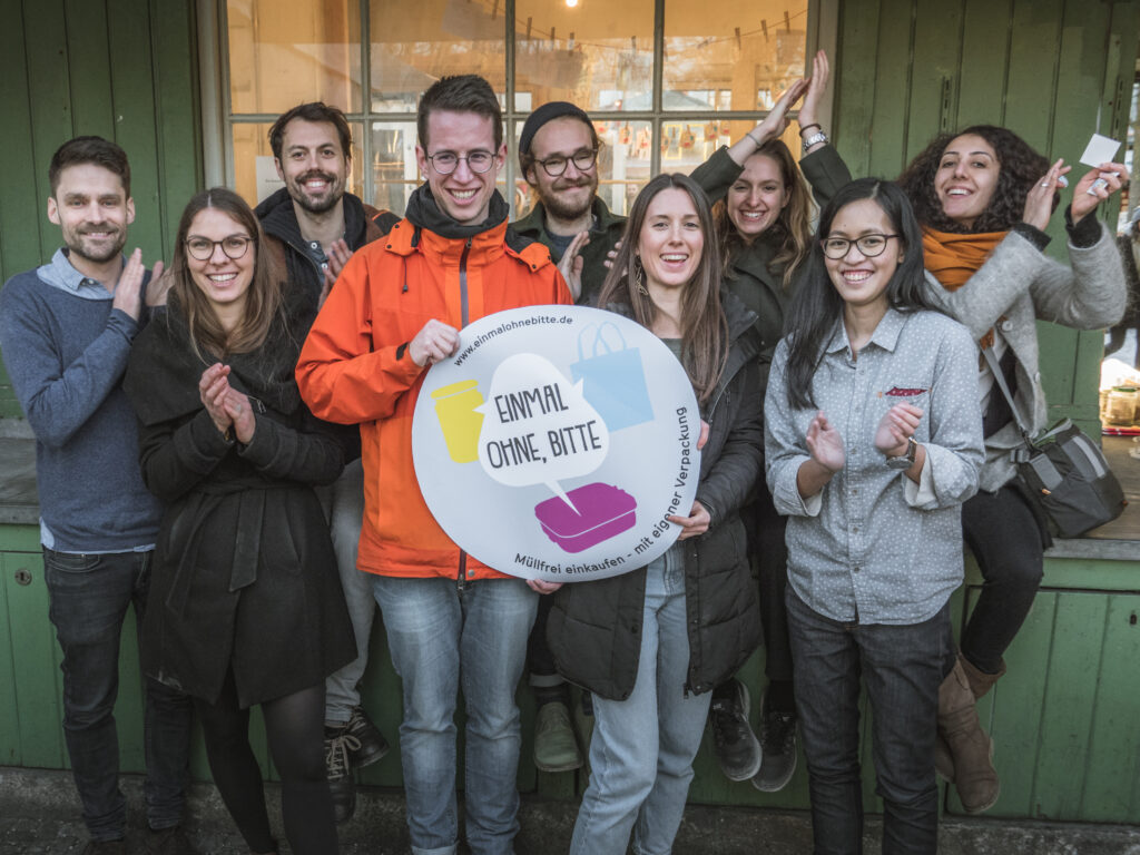 Neun Teammitglieder, die einen Riesensticker von „Einmal ohne, bitte“ hochhalten und jubeln