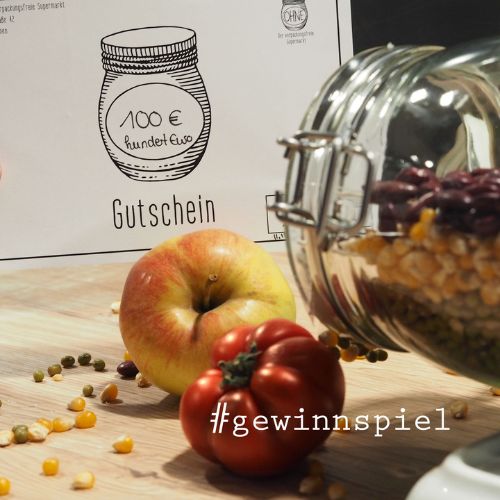 Foto eines 100-€-Gutscheins vom OHNE-Laden auf einem Tisch mit losen Lebensmitteln, davor der Hashtag „#gewinnspiel“